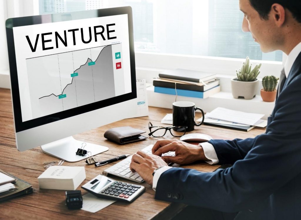 Businessperson viewing a growth chart on a desktop monitor labeled 'VENTURE'