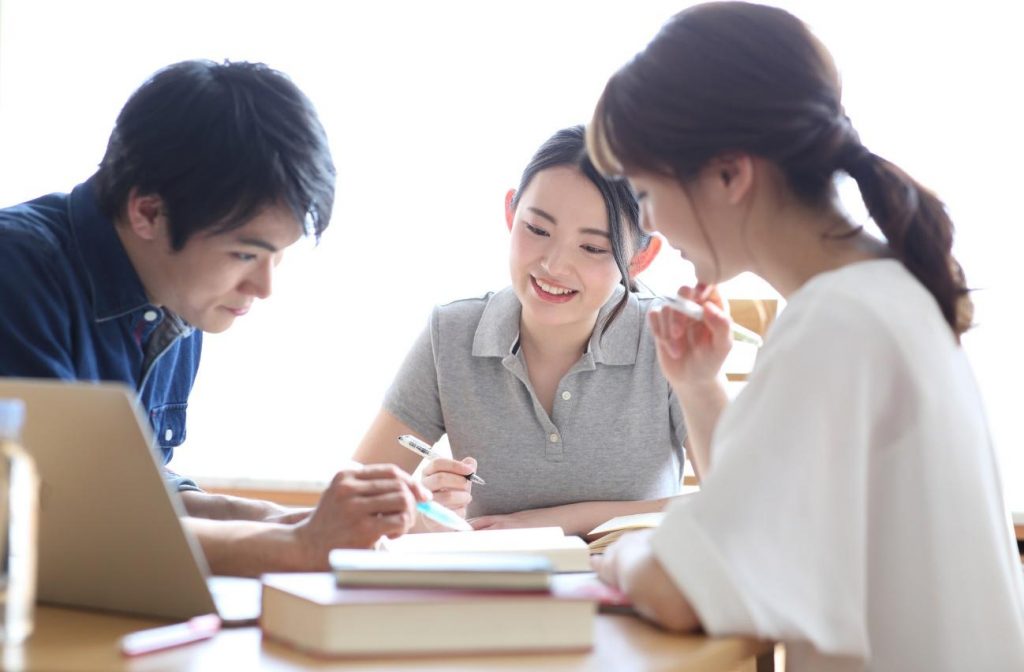 Three students study together at a table, smiling as they review notes; a laptop and books are nearby (informative group study scene).