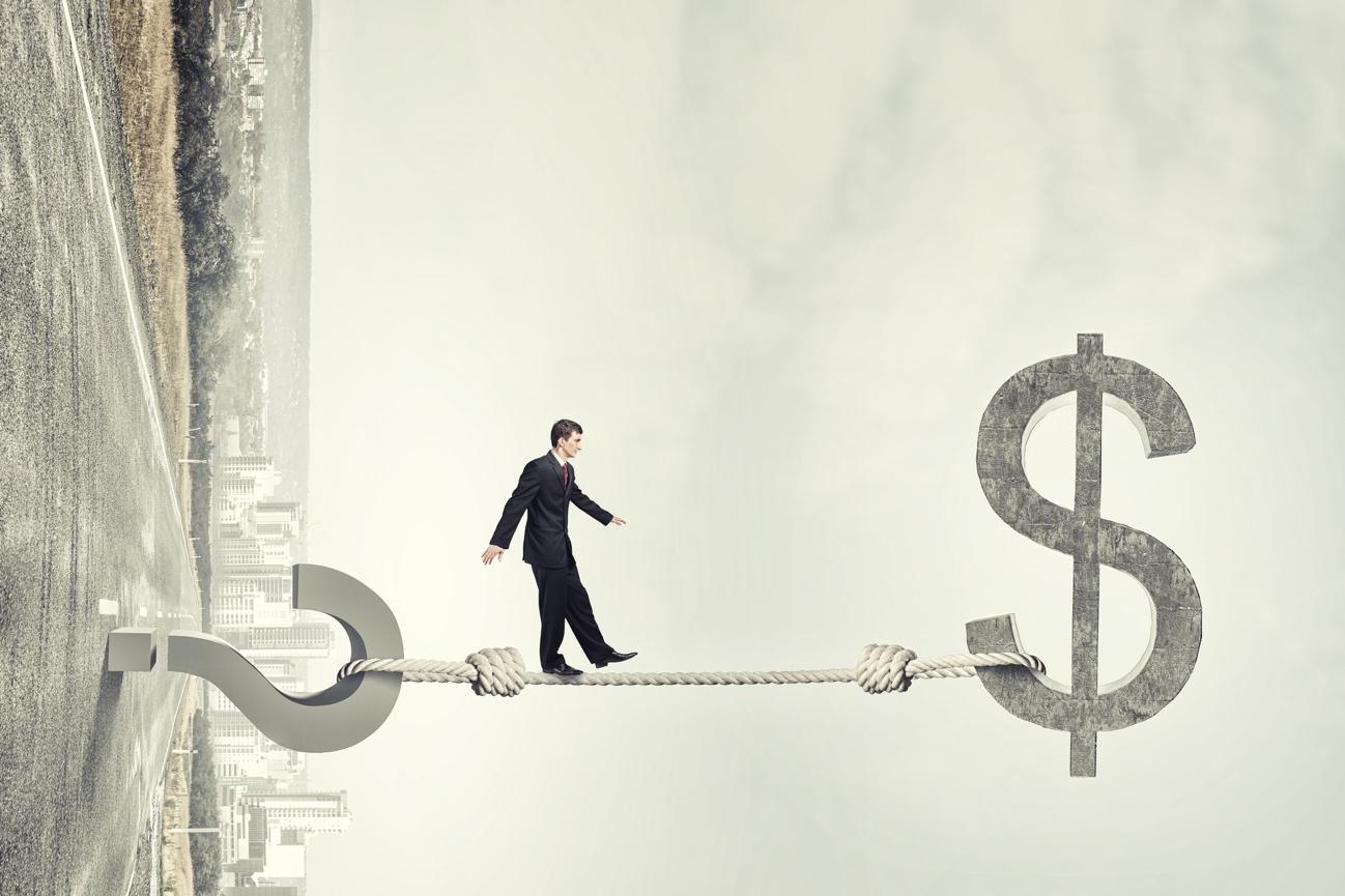 Businessman in a suit walks a rope between abstract financial symbols and a giant dollar sign, symbolizing financial risk.