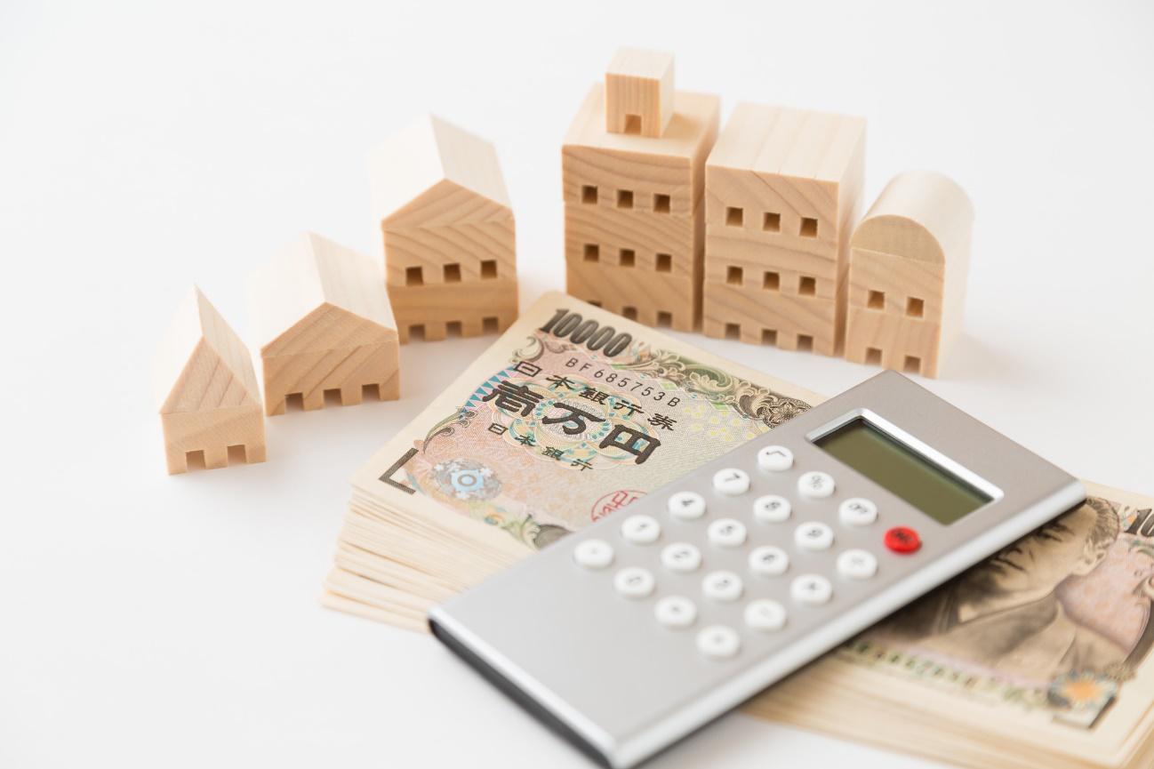 Stack of Japanese yen notes with wooden house models and a calculator, symbolizing real estate investment in Japan.
