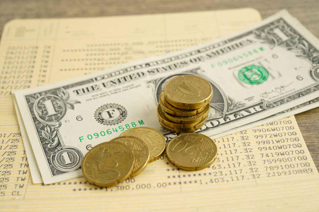 Close-up of stacked coins on top of a one-dollar bill, with more dollars and a financial document in the background.