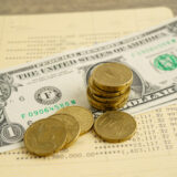 Close-up of stacked coins on top of a one-dollar bill, with more dollars and a financial document in the background.