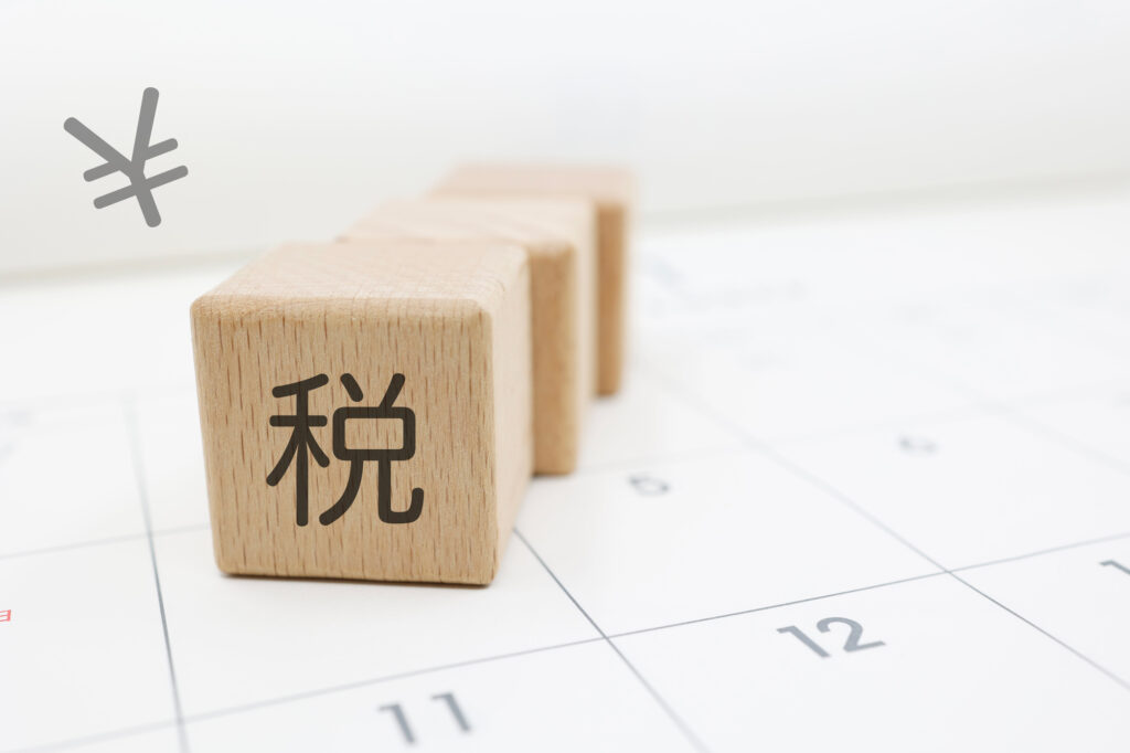 Wooden blocks arranged on a calendar grid, front block showing the Kanji '税' (tax); a gray hash symbol floats to the left.