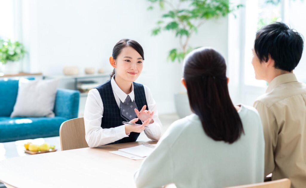 Professional consultant explains something to a couple across a desk in a bright, modern office.