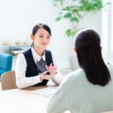 Professional consultant explains something to a couple across a desk in a bright, modern office.