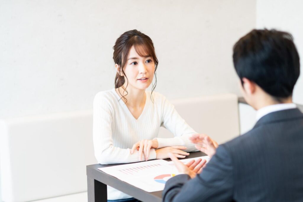 Two professionals sit across a table, discussing documents with a pie chart visible on the papers.