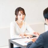 Two professionals sit across a table, discussing documents with a pie chart visible on the papers.