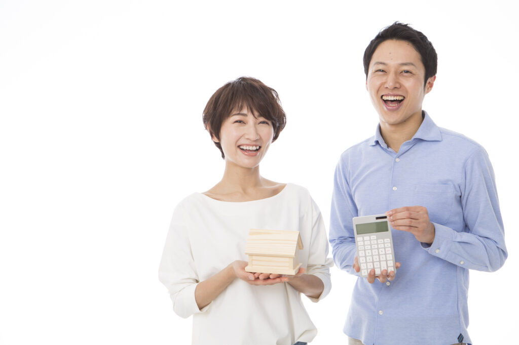 Two smiling adults, a woman holding a small wooden house and a man in a blue shirt holding a calculator, posing happily.