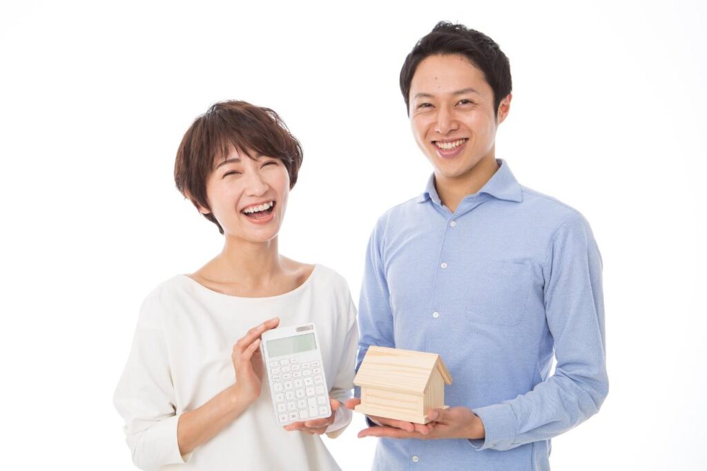 Two smiling adults hold a calculator and a small wooden house model, suggesting home budgeting or mortgage planning.
