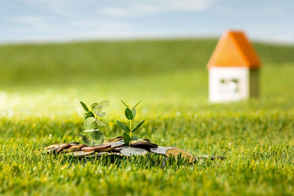 Coins arranged on grass with two small plants sprouting, symbolizing growing savings and future home investment.