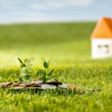 Coins arranged on grass with two small plants sprouting, symbolizing growing savings and future home investment.
