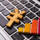Wooden cross and multicolored bar chart resting on a laptop keyboard, implying data visualization in a tech context.