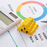 Calculator, gold bullion bars, and a pen on a financial report with a colorful circular chart, suggesting investment analysis.