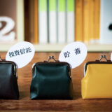 Three small coin purses on a wooden surface, each with a speech bubble label reading 投資信託, 貯蓄, 投資, against a blurred bookshelf background.