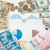 Collage of assorted banknotes and coins surrounding a financial chart with blue bars and a red line.