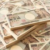 Stacks and scattered 10,000 yen notes featuring Fukuzawa Yukichi, emphasizing wealth imagery on a desk