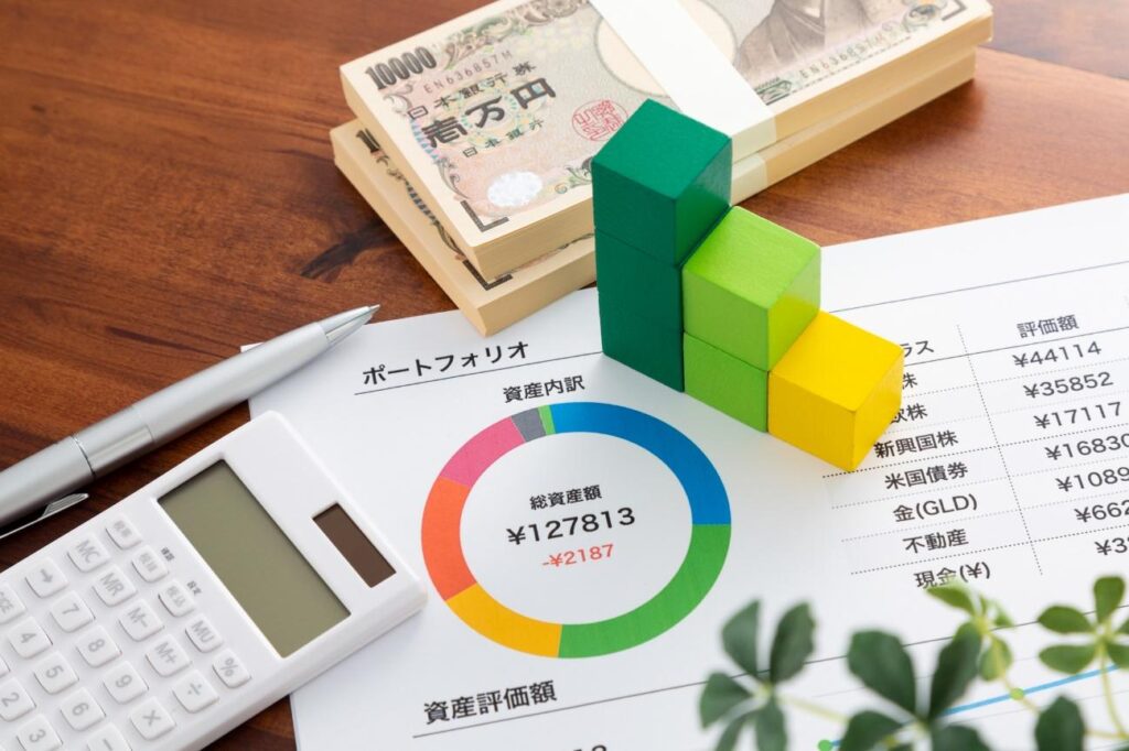 Stacks of 10,000 yen bills beside a multicolored donut chart and a white calculator on a wood desk in a financial setup.