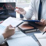 Professionals in a meeting reviewing stock charts on a laptop with notes and reports on the table