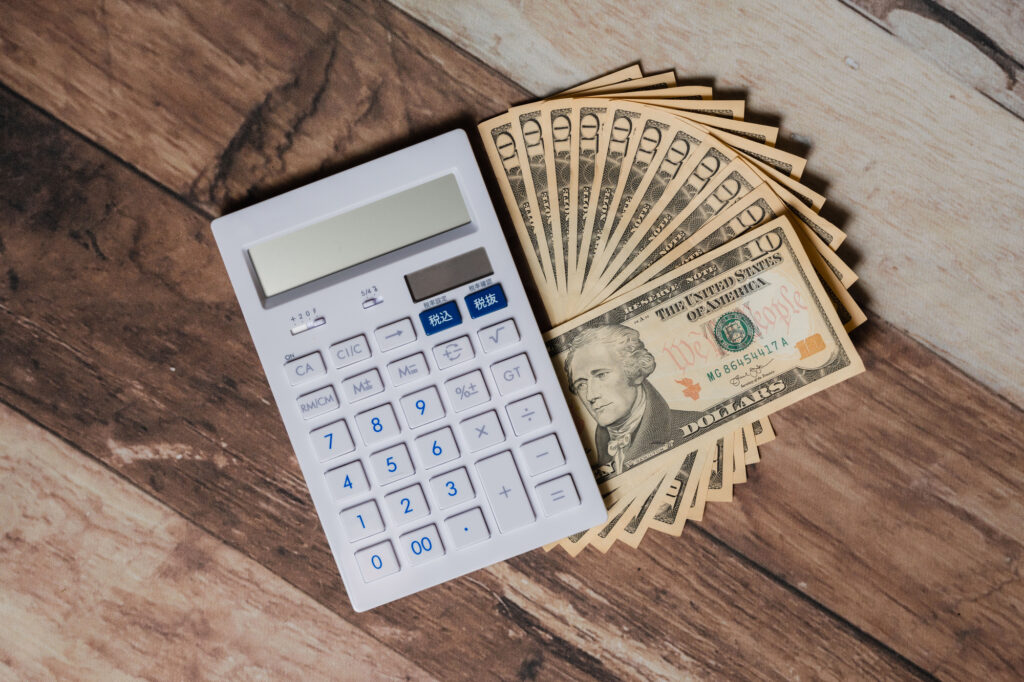 White calculator with blue buttons next to a fan of one-dollar bills on a wooden surface