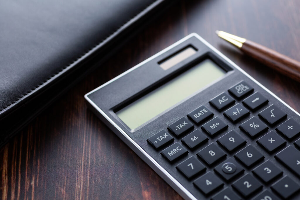 Close-up of a gray calculator on a dark wooden desk, with a brown-and-gold pen nearby